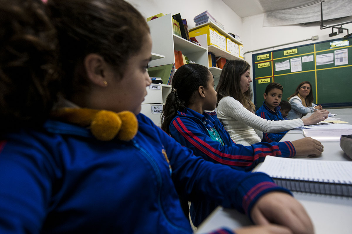 Imagem de crianças sentadas a mesa conversando com uma professora