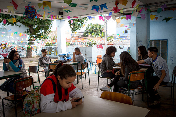 Alunos sentados em grupos de até 4, em pátio externo