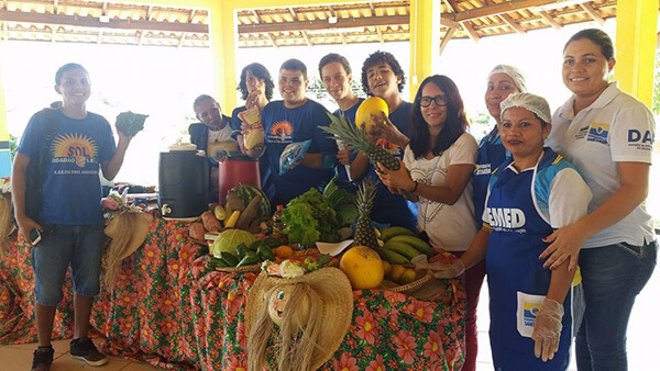 Mesa com frutas, legumes e vegetais, alunos e funcionários em volta da mesa